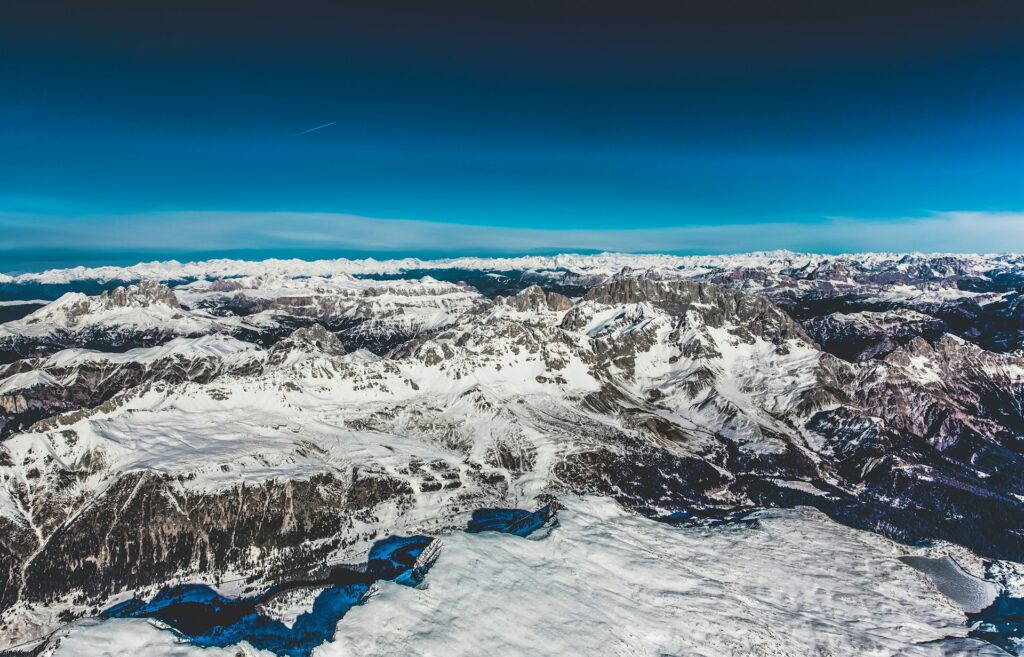 drone shot of the alps in italy. showcasing the number 1 item on your italy bucket list. massive mountain ranges for as far as the eye can see. crystal clear blue skies above.