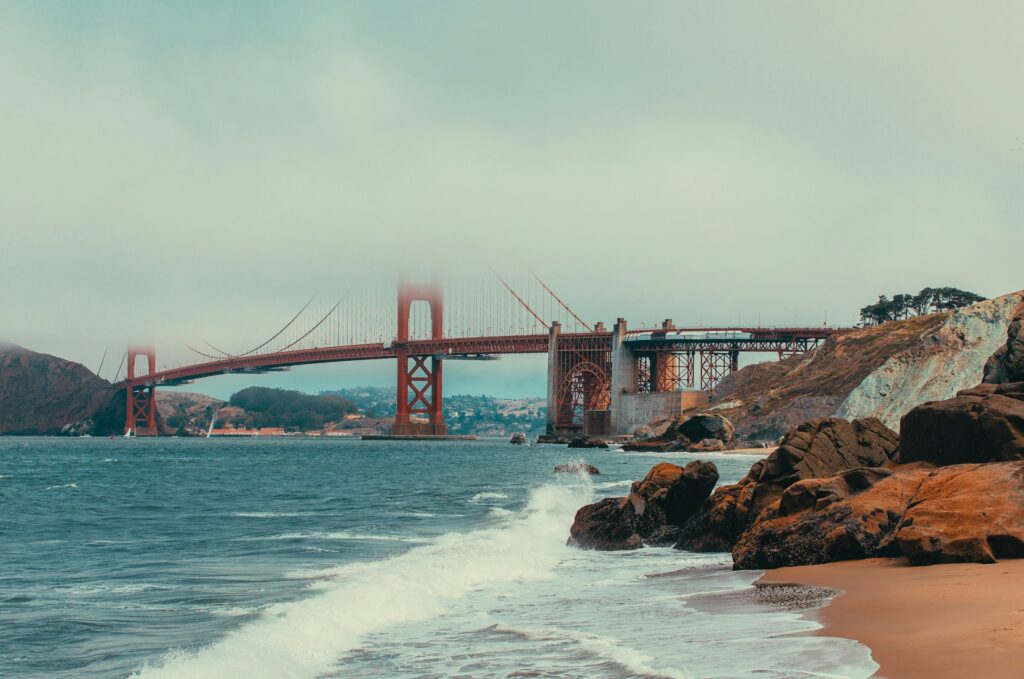 beach view to the golden gate bridge. clouds covering the top half of the bridge. waves crashing on the shore. a must see for one day in san francisco.