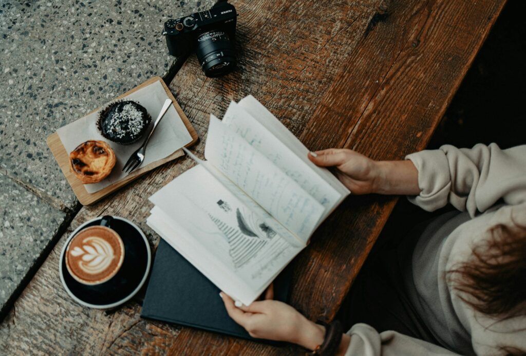 an overhead shot of someone reading a book with a coffee and a couple pastries. showcasing one of the places to get the best pastel de nata in lagos.