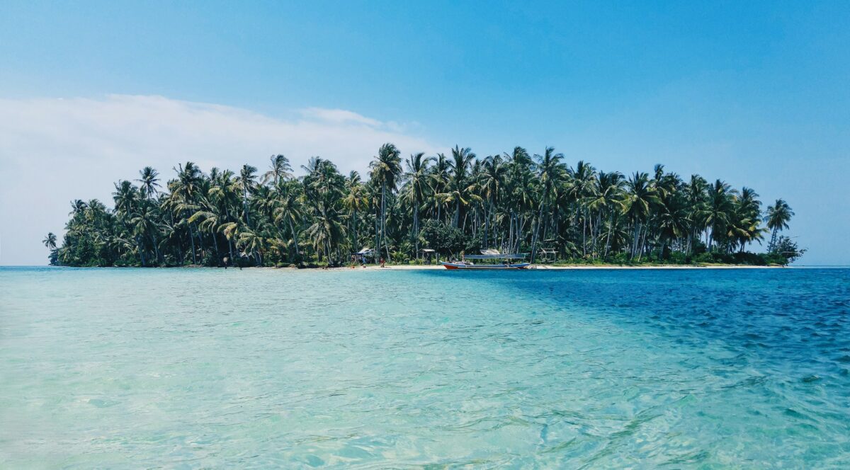 Beautiful island in the Mentawai Islands with crystal-clear blue water, white sand beach, and lush palm trees, showcasing the best things to do in the Mentawai Islands.