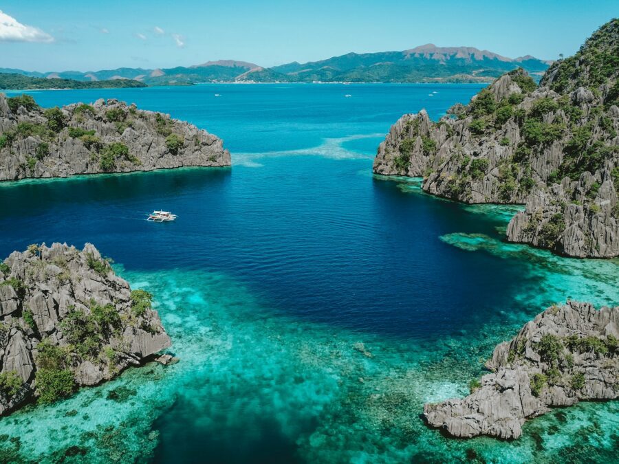 Crystal-clear blue waters surrounding rocks in Palawan, with a boat floating nearby, showcasing the beauty of the island, perfect for a 7 day Palawan itinerary.