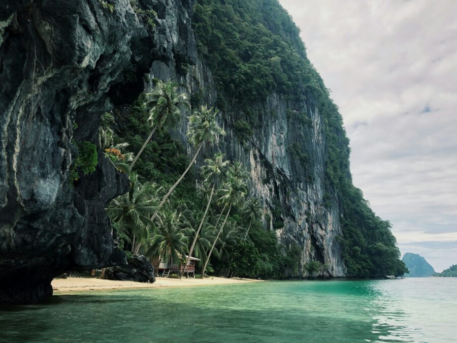 Pristine blue waters and a white sand beach surrounded by lush jungle mountains, showcasing one of the best places to snorkel in Palawan.
