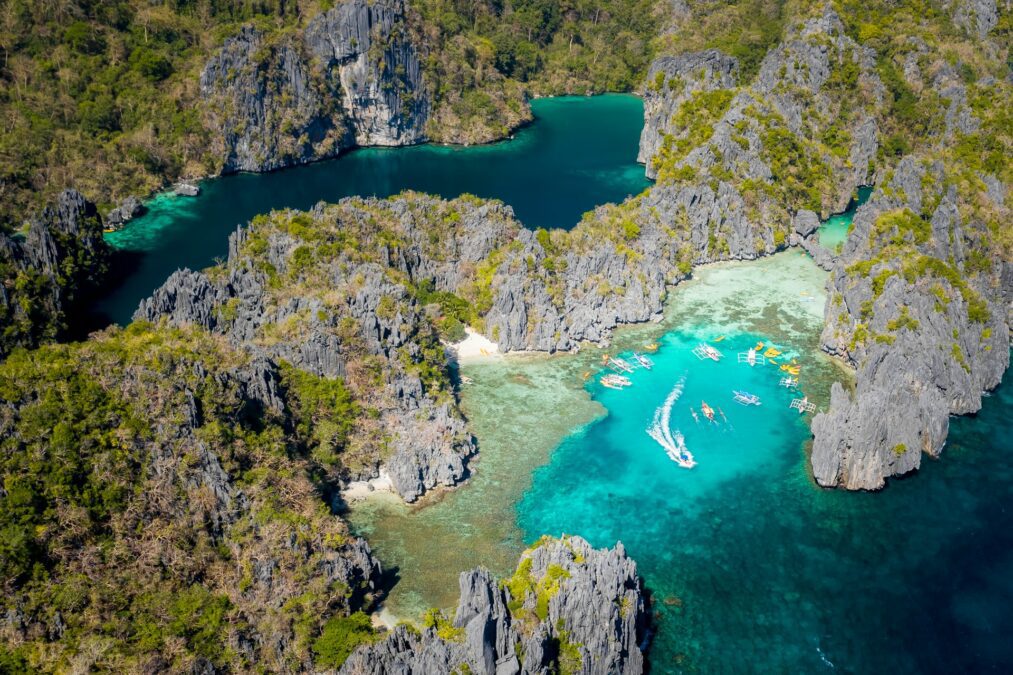 Overview of El Nido and neighboring islands with crystal-clear blue waters and a boat docked on a small beach. A stunning scene showcasing the beauty and top things to do in El Nido.